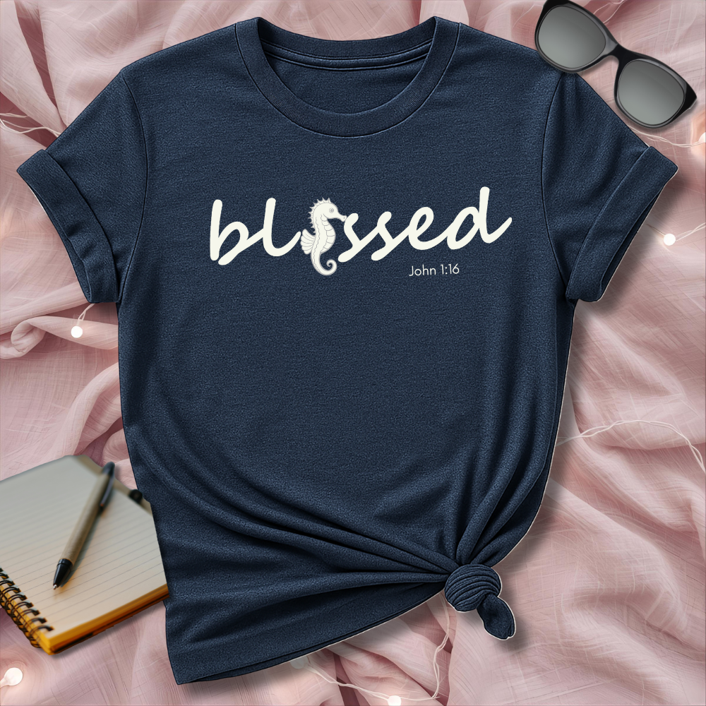 Navy blue t-shirt with 'blessed' text on a pink surface with sunglasses and notebook.