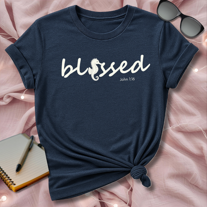 Navy blue t-shirt with 'blessed' text on a pink surface with sunglasses and notebook.
