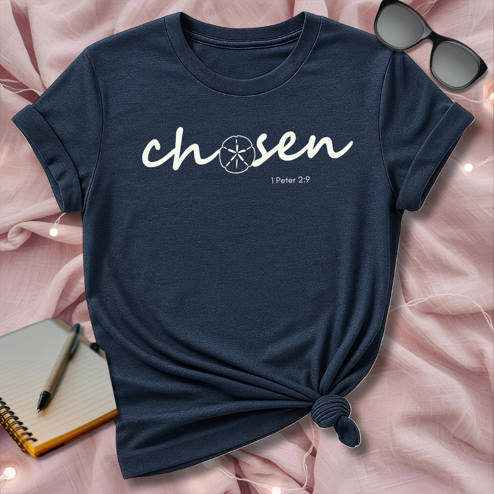 Navy blue t-shirt with 'chosen' text on a pink surface with sunglasses and notebook.