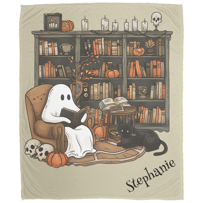 Blanket with a ghost reading a book and a black cat in front of a bookshelf with Halloween decorations.