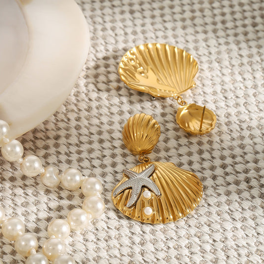 Gold shell earrings with a starfish detail on a textured surface with pearls.
