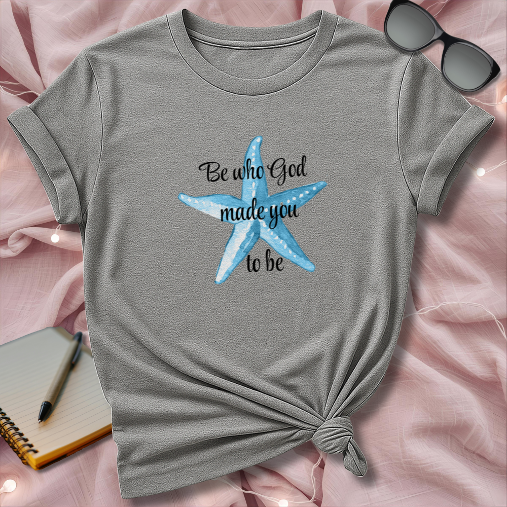Gray t-shirt with blue starfish design and text on a pink surface with sunglasses and notebook.