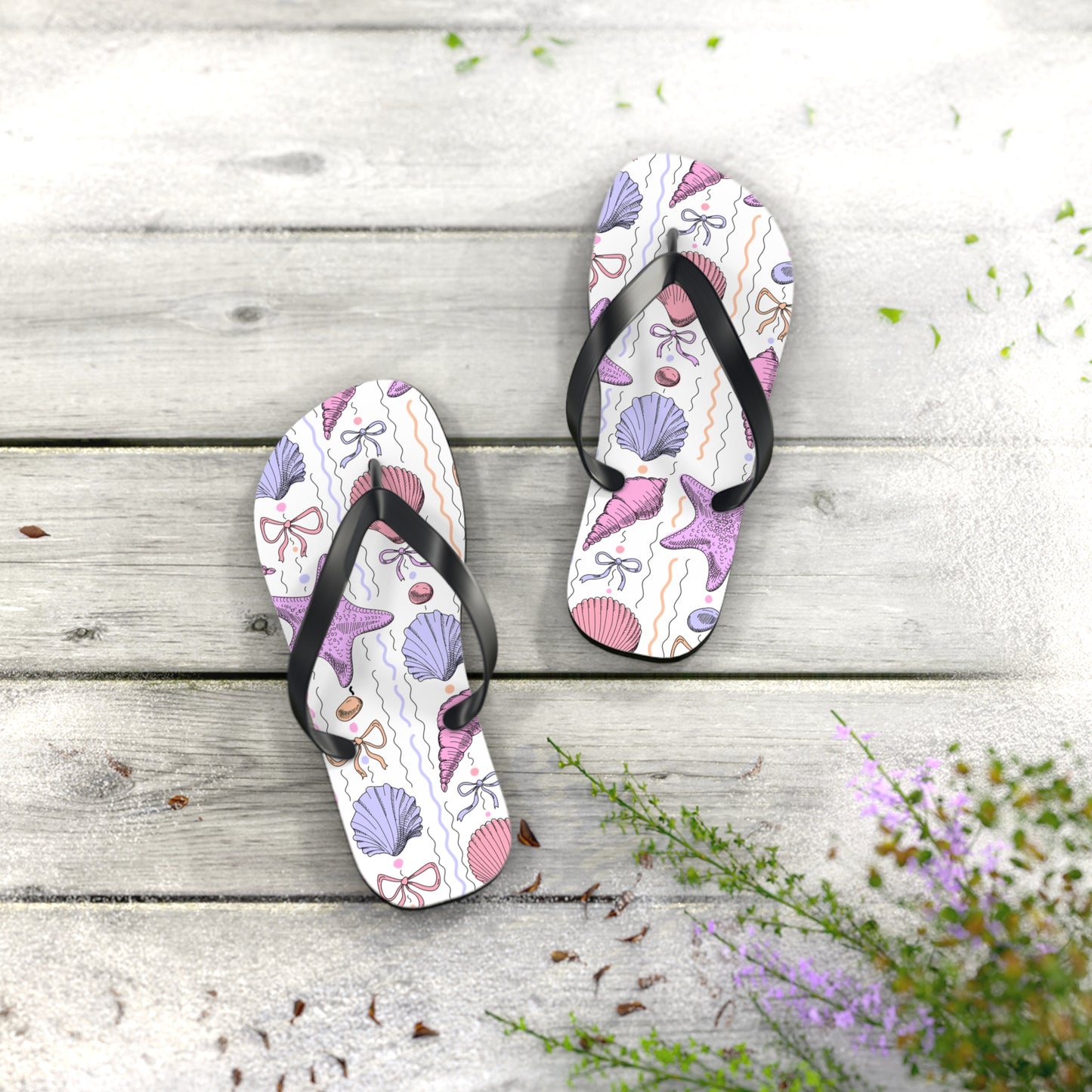 Pair of flip-flops with a shell pattern on a wooden surface with flowers.