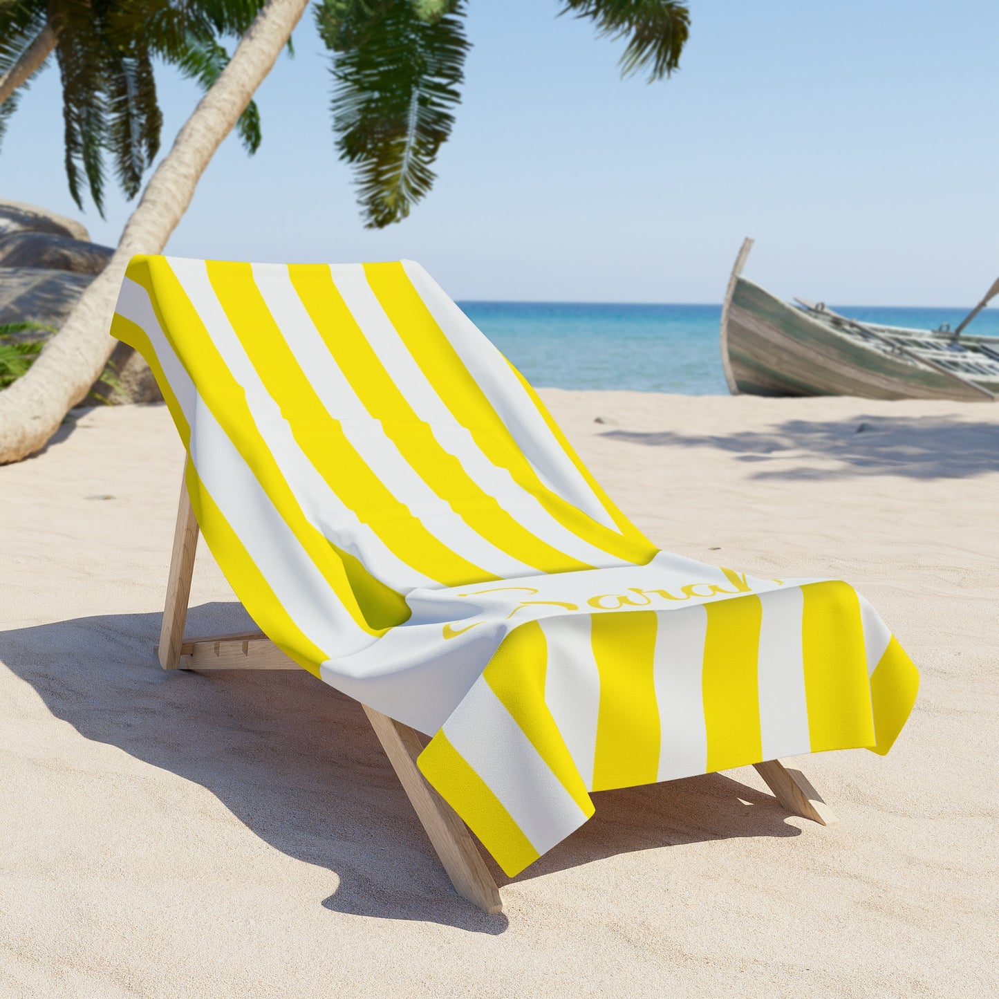 Yellow and white striped towel draped over a beach chair on a sandy beach with palm trees and ocean in the background.