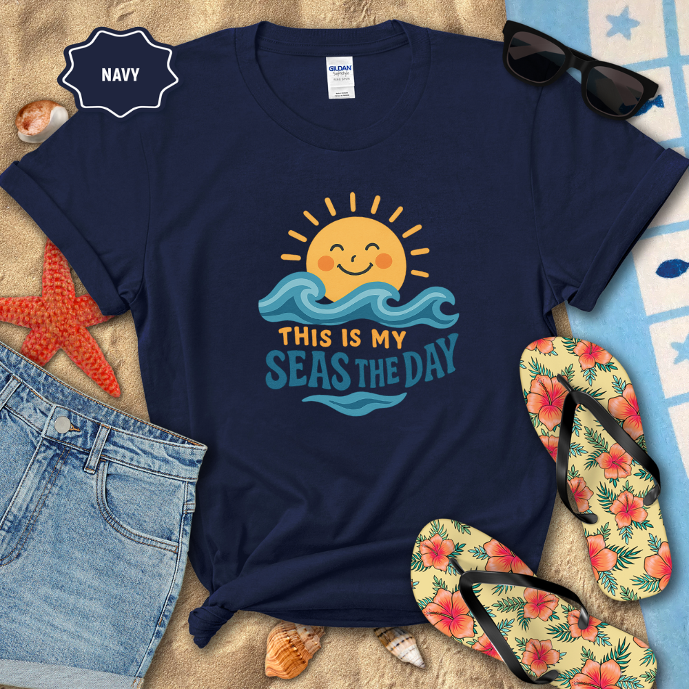 Navy t-shirt with beach-themed design on a sandy surface with flip-flops and sunglasses.