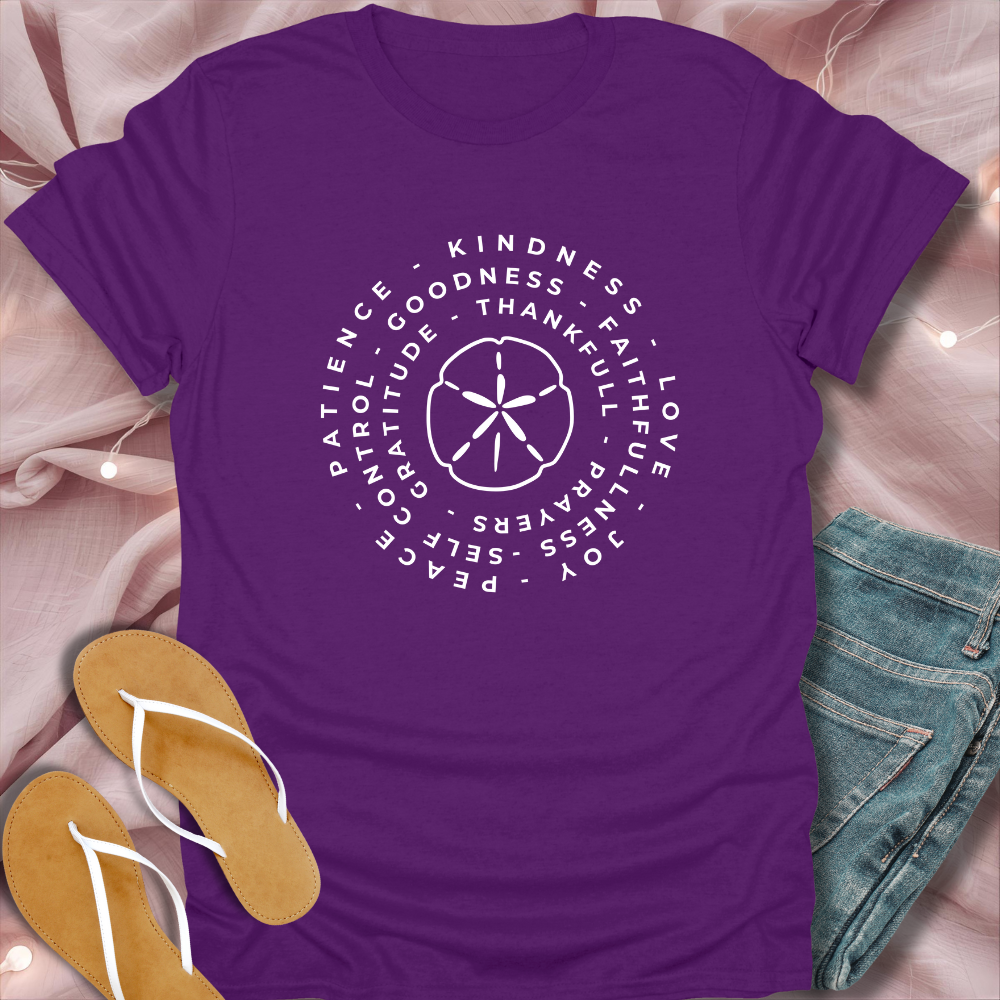 Purple t-shirt with white text and design on a pink surface with sandals and jeans.