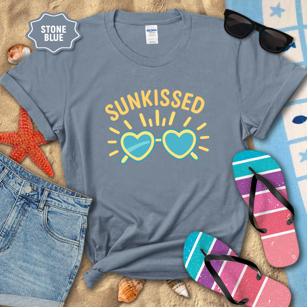 Blue t-shirt with 'Sunkissed' design on a sandy background with beach accessories.