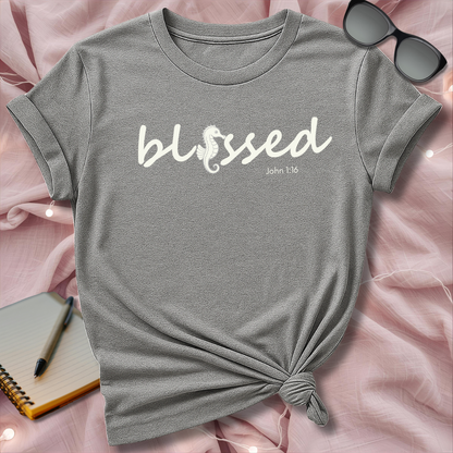 Gray t-shirt with 'blessed' text on a pink surface with sunglasses and notebook.
