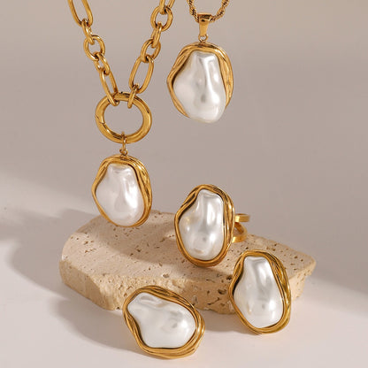 Irregular pearl necklace, earrings, and ring set in gold on neutral stone background

