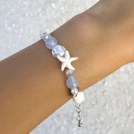 Bracelet with starfish and shell design on a wrist against a textured white background