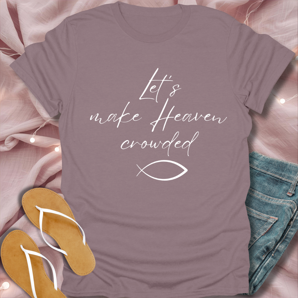 Purple t-shirt with 'Let's make Heaven crowded' text and fish symbol on a pink fabric background.
