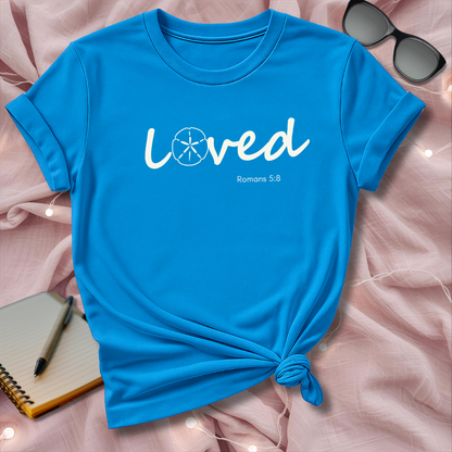 Blue t-shirt with 'loved' text on a pink surface with sunglasses and notebook.