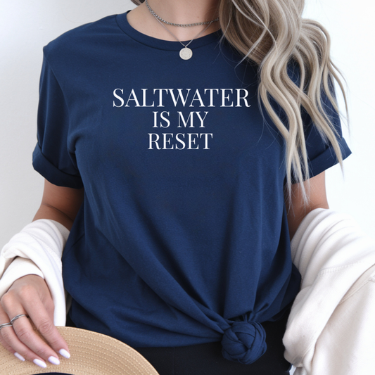 Person wearing a navy blue t-shirt with 'SALTWATER IS MY RESET' text.
