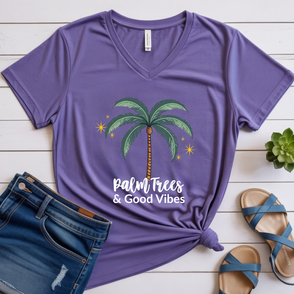 Purple t-shirt with palm tree design and 'Palm Trees & Good Vibes' text on a wooden surface with jeans and sandals.