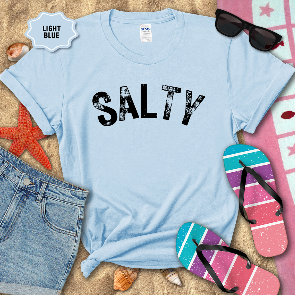 Light blue t-shirt with 'SALTY' text on a sandy background with beach accessories.