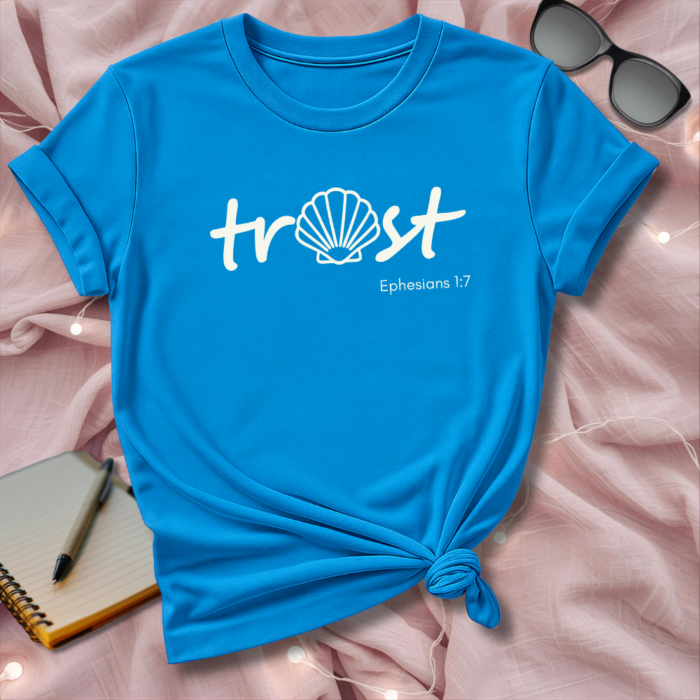 Blue t-shirt with 'trust' and shell design on a pink surface