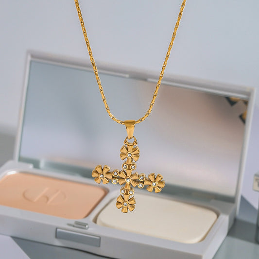 Gold cross necklace with floral designs on a makeup compact background
