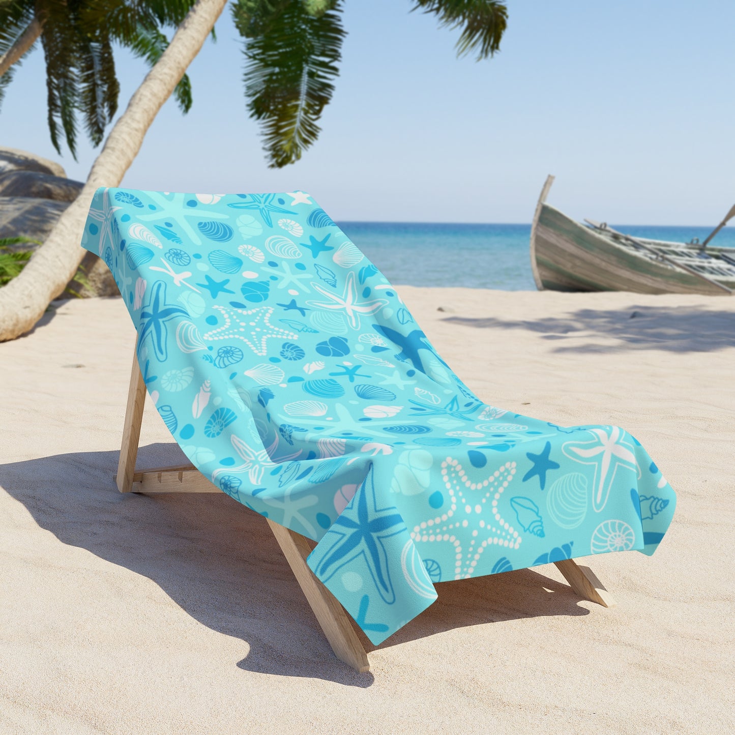 Beach towel with sea-themed design on a wooden chair on a sandy beach.