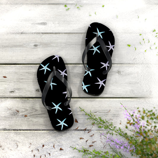 Black flip-flops with starfish pattern on a wooden surface with flowers.