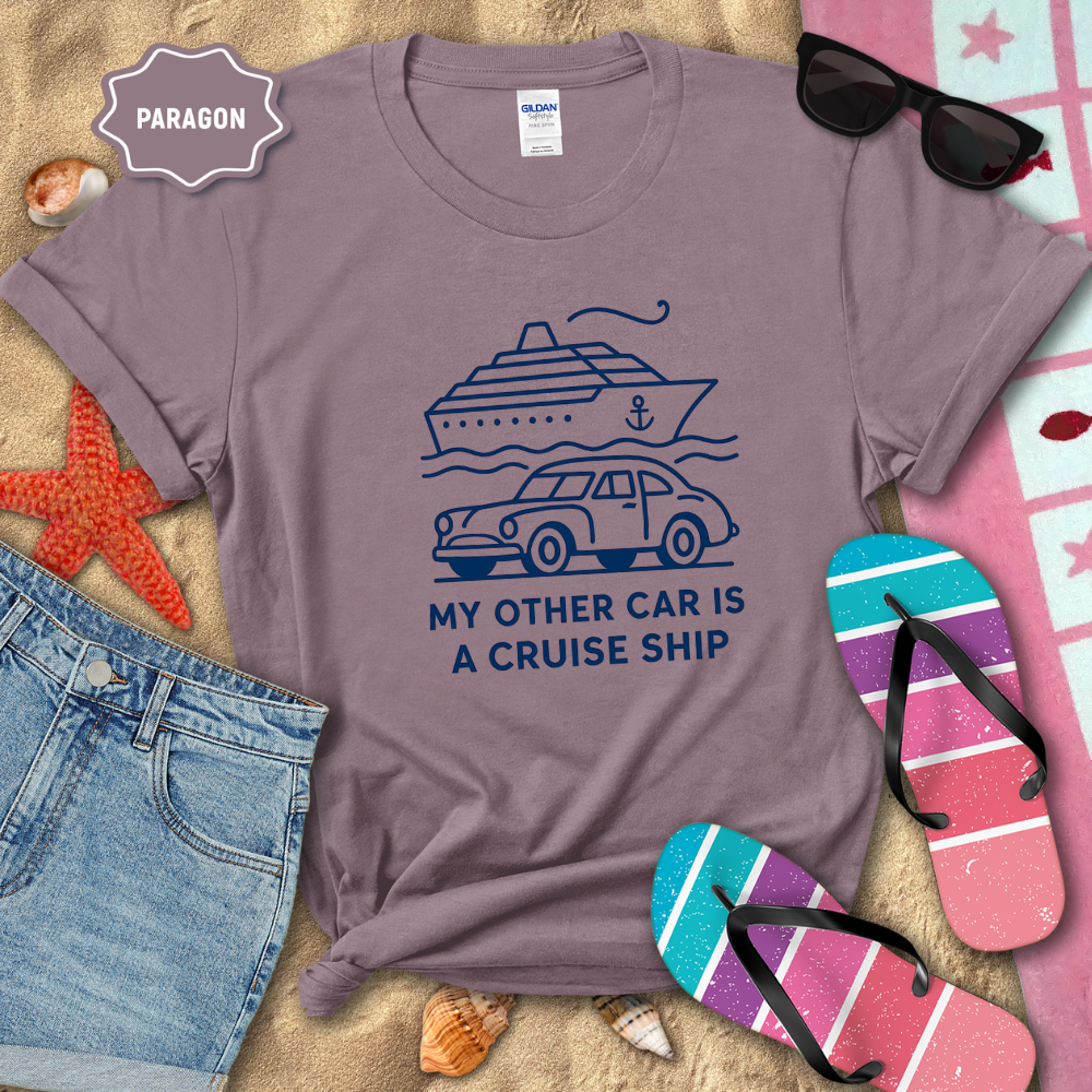 Purple t-shirt with a graphic design and text, surrounded by beach items on sand.