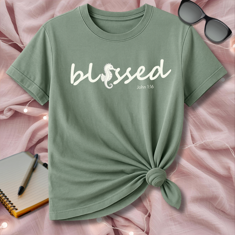Green t-shirt with 'blessed' text on a pink surface with sunglasses and notebook.