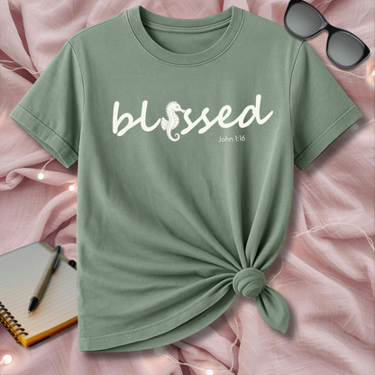 Green t-shirt with 'blessed' text on a pink surface with sunglasses and notebook.