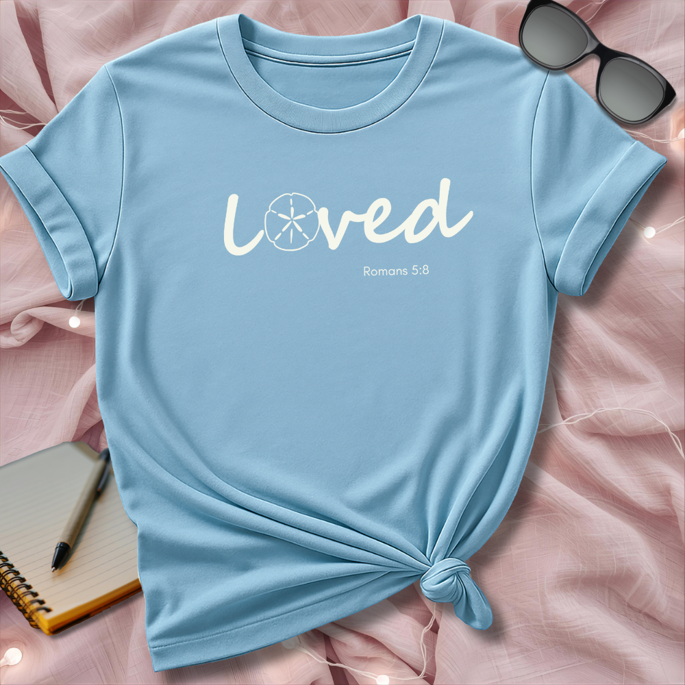 Light blue t-shirt with 'Loved' text on a pink surface with sunglasses and notebook.