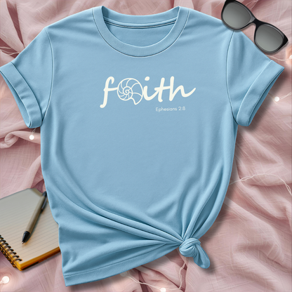 Light blue t-shirt with 'faith' text on a pink surface with sunglasses and notebook.
