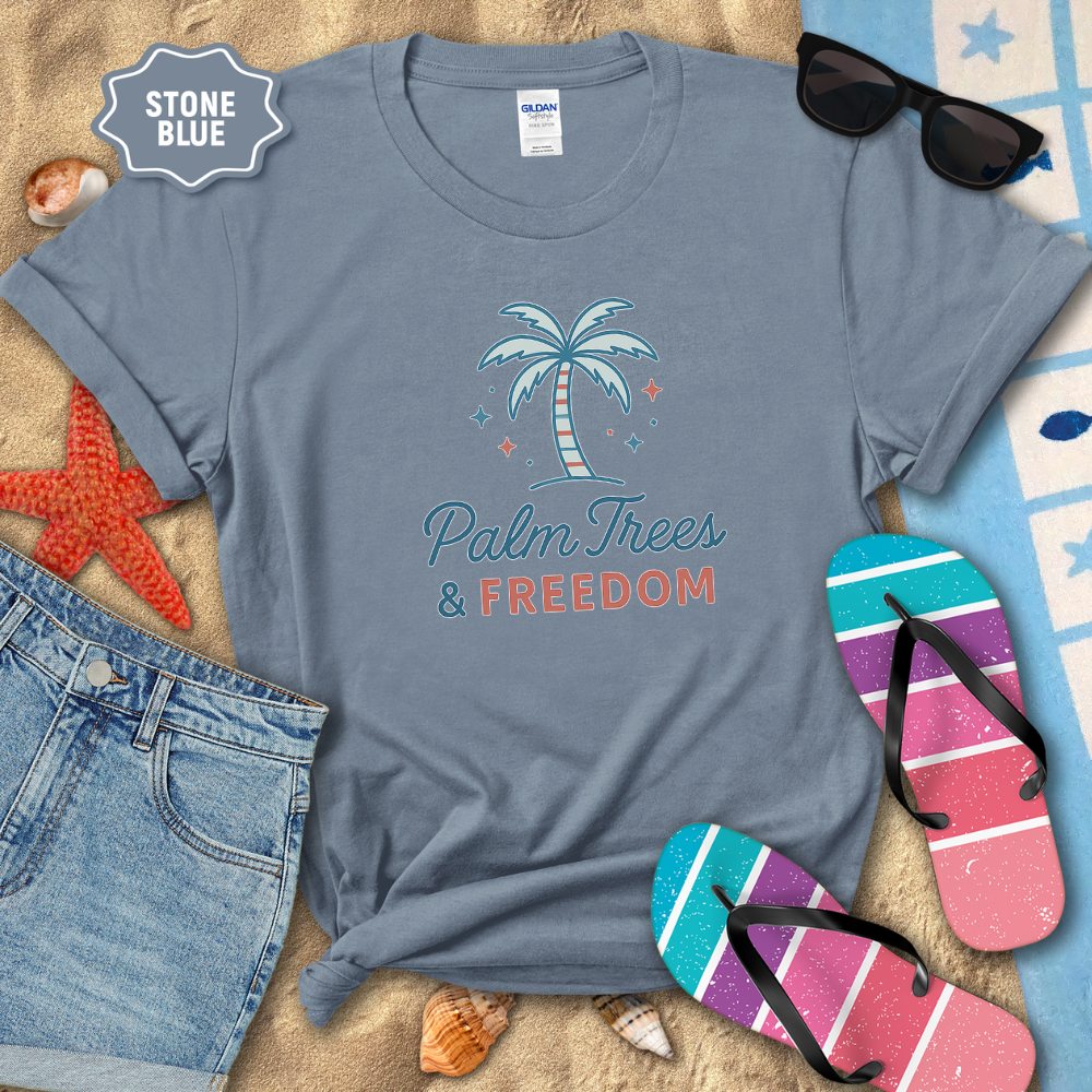 Stone blue t-shirt with palm tree and 'Palm Trees & Freedom' text on a sandy background with beach accessories.