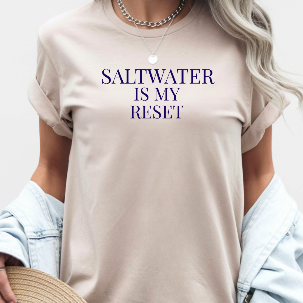 Person wearing a beige t-shirt with 'SALTWATER IS MY RESET' text on a light background