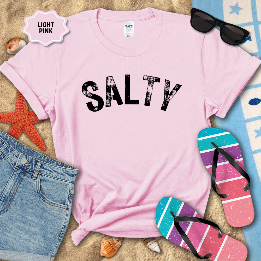 Light pink t-shirt with 'SALTY' text on a beach-themed background with sunglasses, flip-flops, and denim shorts.