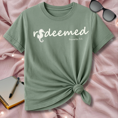 Green t-shirt with 'redeemed' text on a pink surface with sunglasses and notebook.