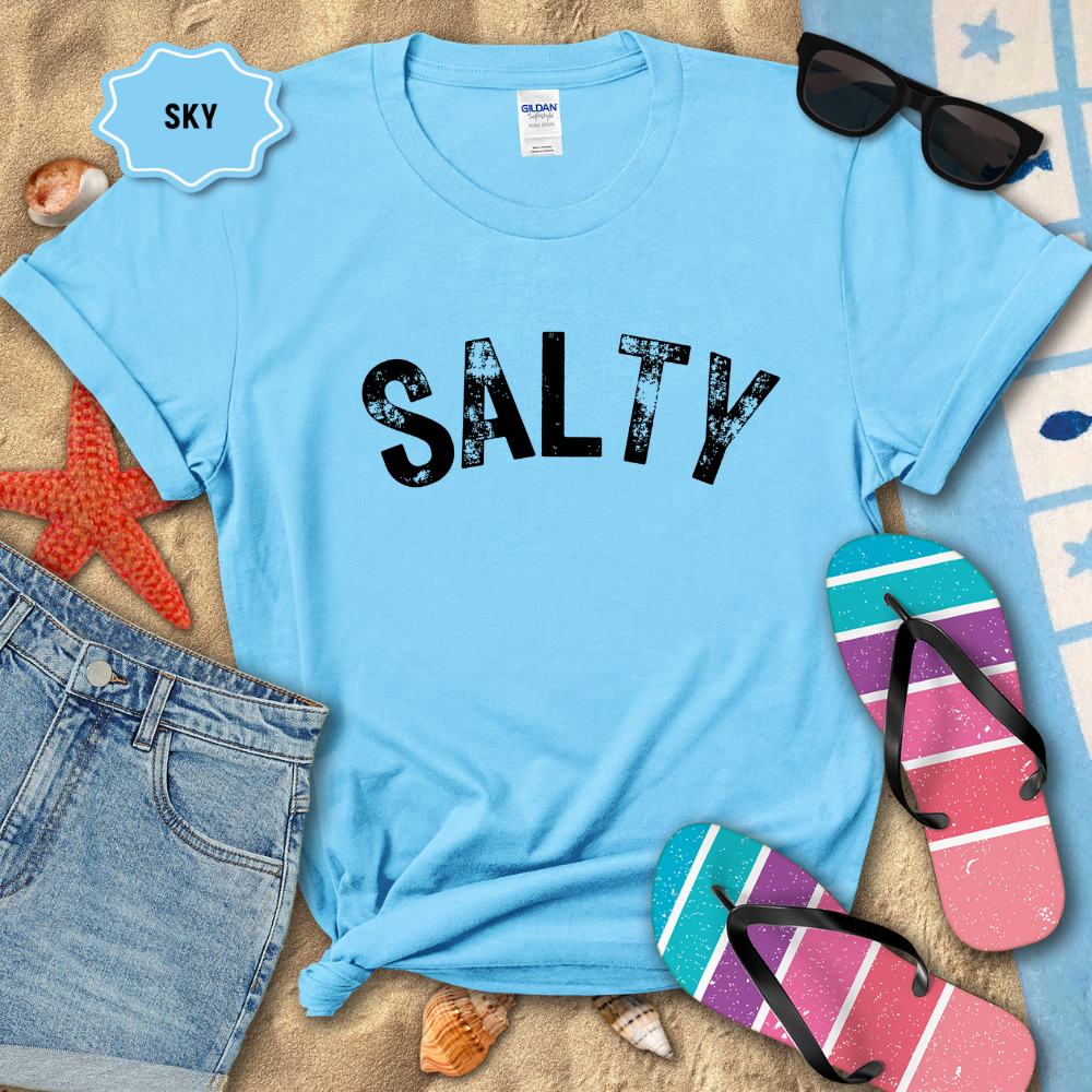 Light blue t-shirt with 'SALTY' text on a sandy background with beach accessories.