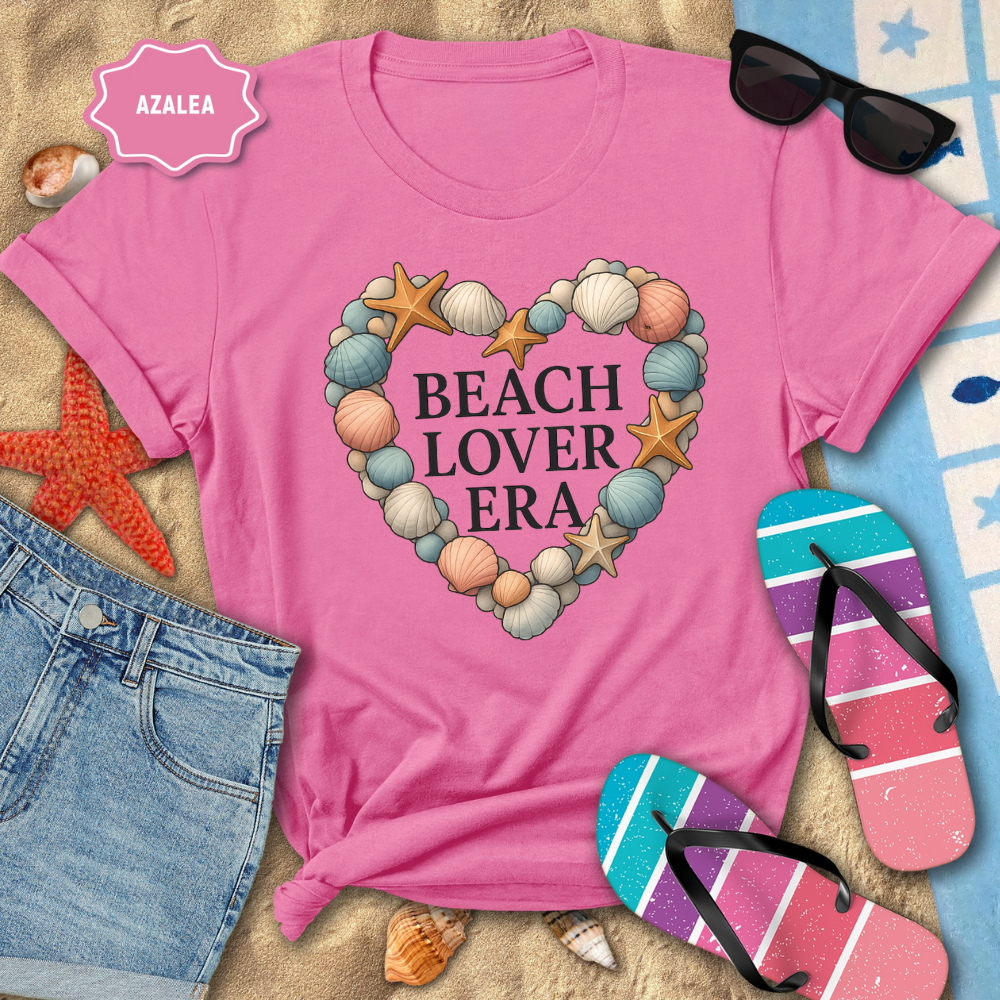 Pink t-shirt with 'Beach Lover Era' design on a sandy background with beach accessories.