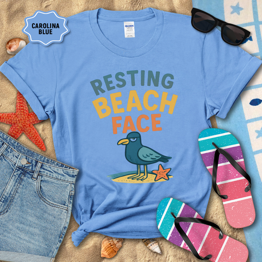 Blue t-shirt with 'Resting Beach Face' design on a sandy background with beach accessories.