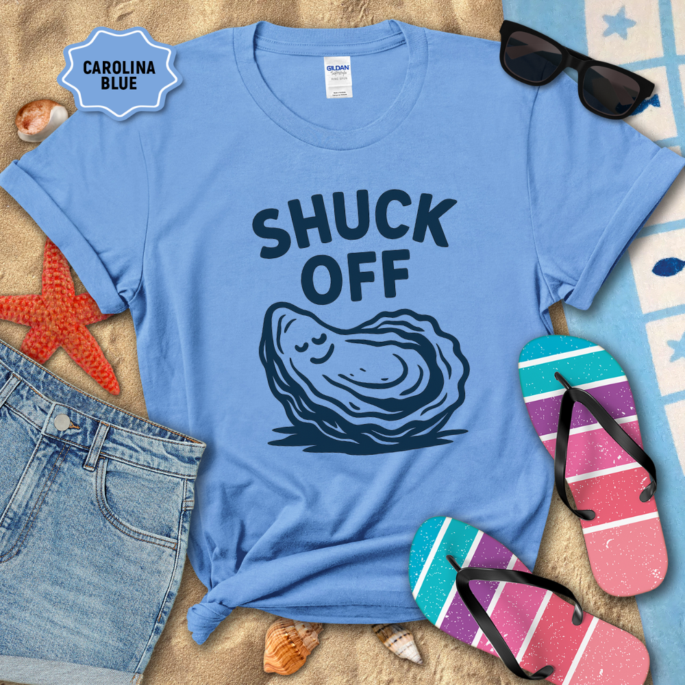 Blue t-shirt with 'SHUCK OFF' graphic and oyster illustration on a beach setting with sunglasses, flip-flops, and starfish.