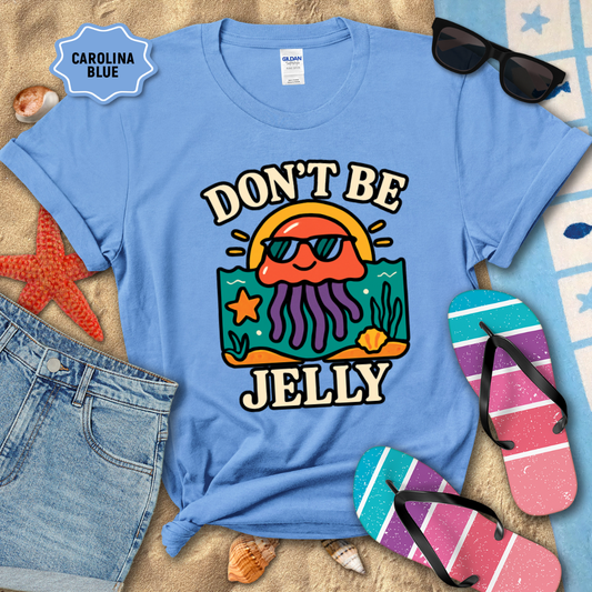 Light blue t-shirt with 'Don't Be Jelly' design on a sandy background with beach accessories.