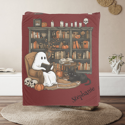 Blanket with ghost reading a book design, featuring 'Stephanie' on a wooden floor.