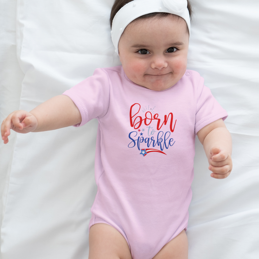 Smiling baby in a light pink “Born to Sparkle” bodysuit with red, white, and blue patriotic design, lying on a white blanket.
