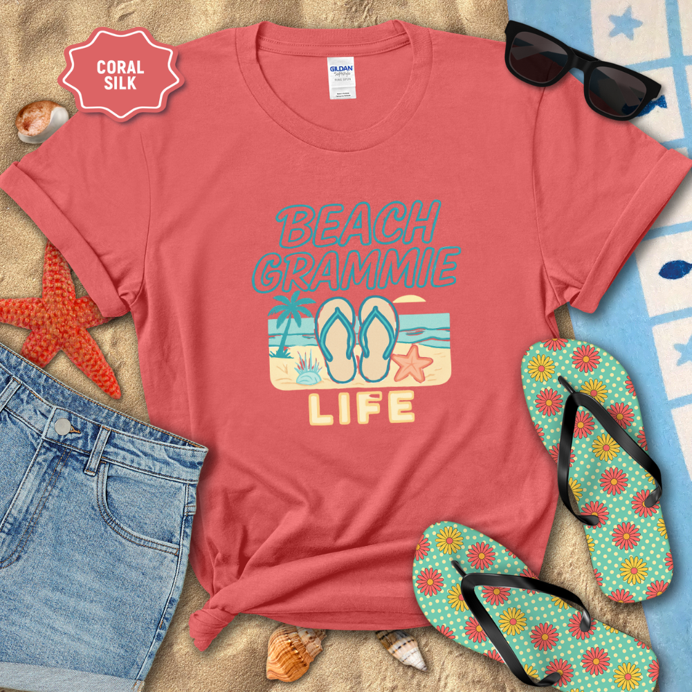 Coral t-shirt with 'Beach Grammie Life' design on a sandy background with flip-flops and sunglasses.