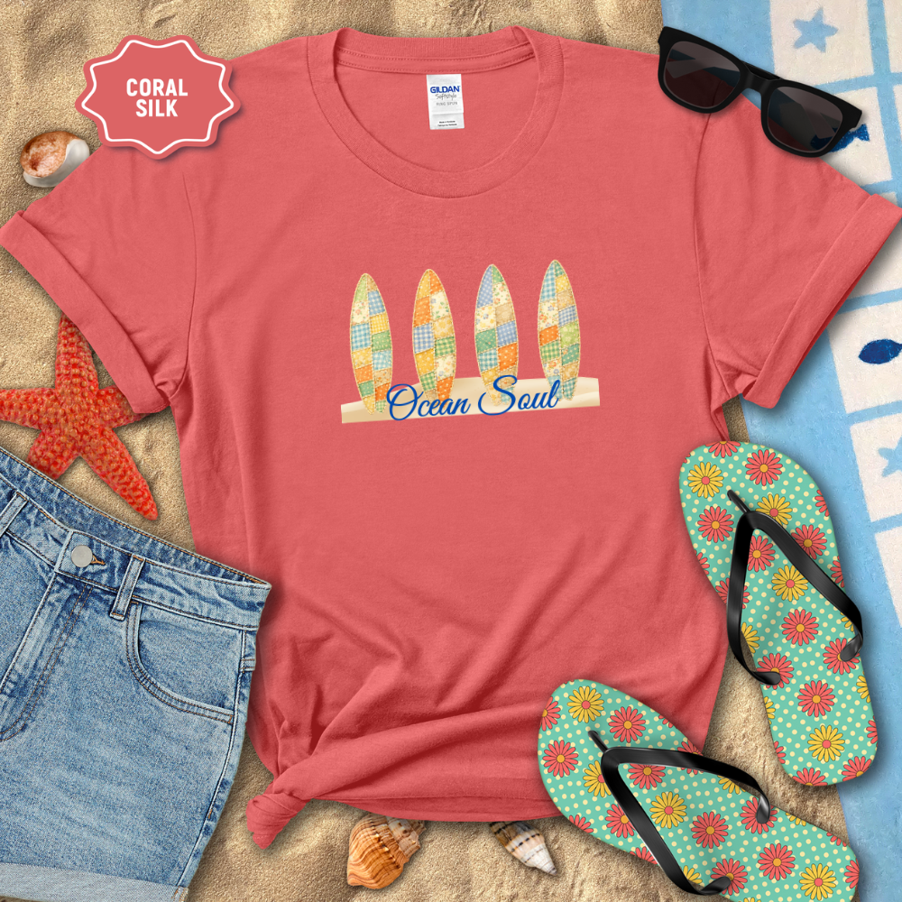 Coral t-shirt with 'Ocean Soul' design on a beach setting with sunglasses, flip-flops, and denim shorts.
