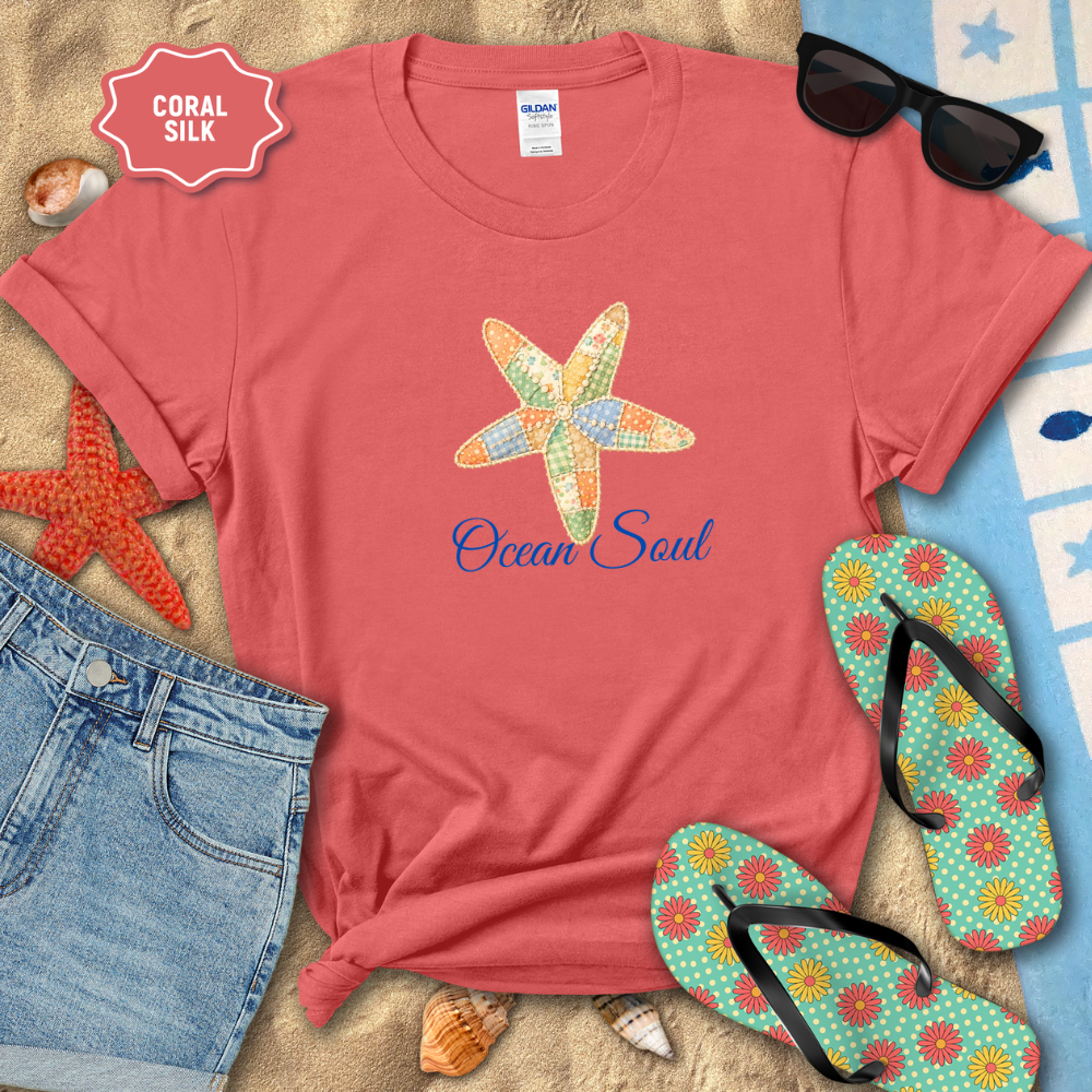Red t-shirt with starfish design and 'Ocean Soul' text, surrounded by beach accessories on sand.