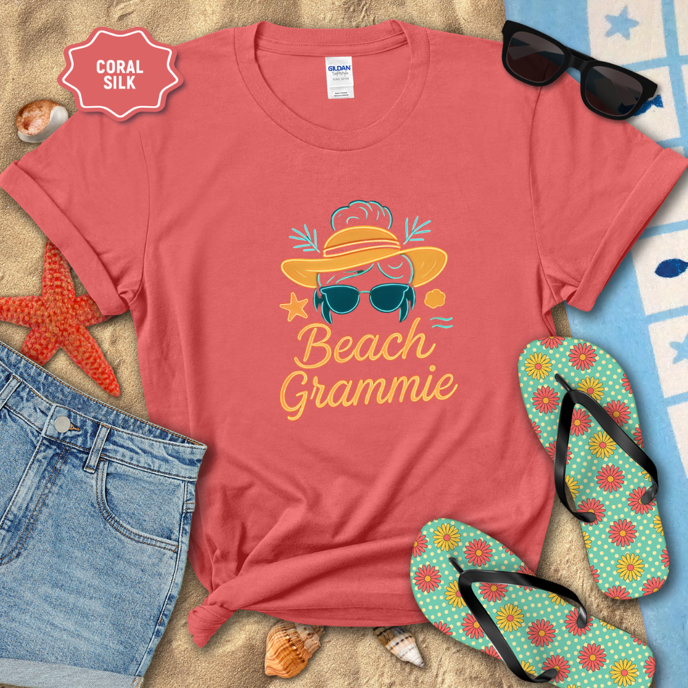 Coral t-shirt with 'Beach Grammie' design on a sandy background with flip-flops and sunglasses.