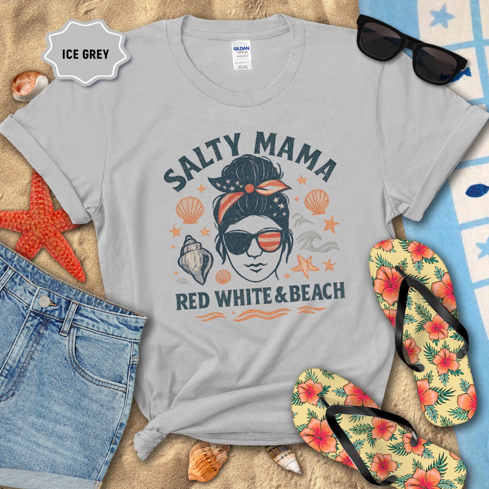 Gray t-shirt with 'Salty Mama Red White & Beach' design on sand with sunglasses, flip-flops, and denim shorts.