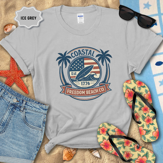Gray t-shirt with 'Coastal Freedom Beach Co' design on sand with beach accessories.