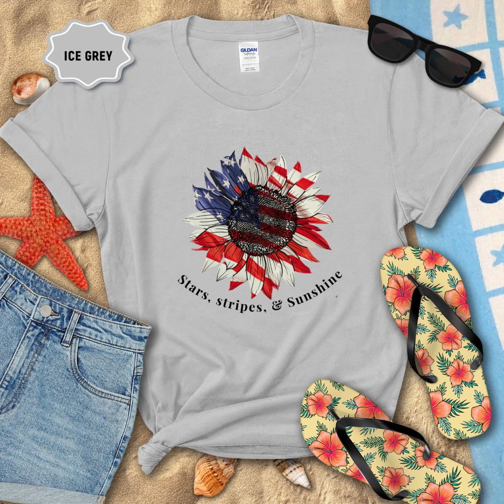 Gray t-shirt with sunflower design and text on a sandy background with beach accessories.