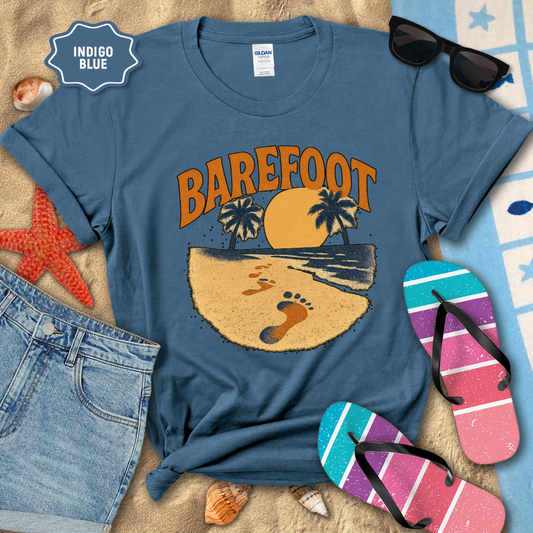 Indigo blue t-shirt with 'Barefoot' graphic design on a sandy surface with beach accessories.