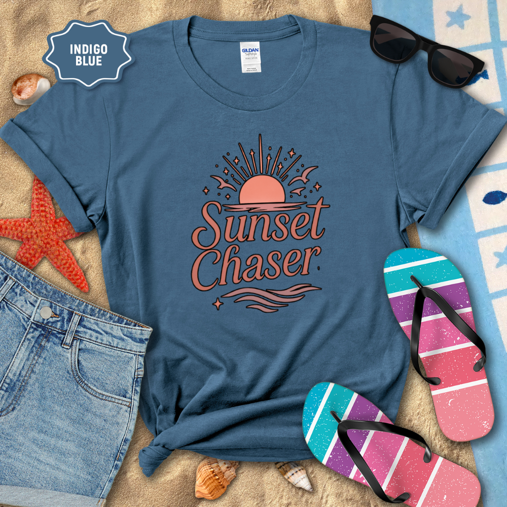 Blue t-shirt with 'Sunset Chaser' design on a beach setting with sunglasses, flip-flops, and denim shorts.
