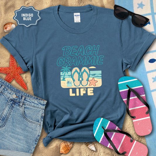 Indigo blue t-shirt with 'Beach Grammie Life' design on a sandy background with flip-flops and sunglasses.