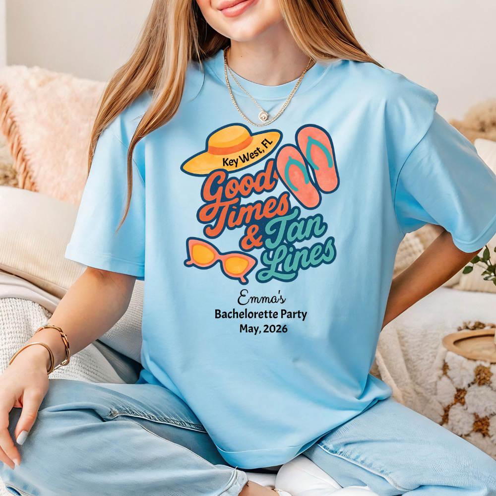 Person wearing a light blue t-shirt with 'Good Times & Tan Lines' design, sitting on a couch.